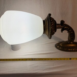 May include: A white frosted glass lampshade with a decorative gold metal base and arm. The lampshade is shaped like a teardrop and the base has intricate details.