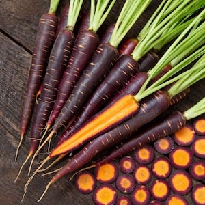 Peut inclure: Un bouquet de carottes violettes avec un intérieur orange. Les carottes sont disposées sur une surface en bois avec quelques carottes tranchées au premier plan.