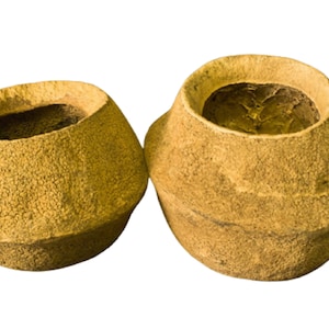 May include: Two beige, textured, bowl-shaped objects with wide openings. The objects have a rough, organic appearance, possibly made from natural materials. The interior of the bowls is a darker shade of brown. The background is plain white.
