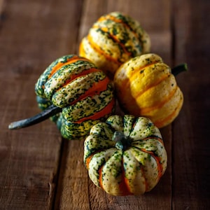 Peut inclure: Plusieurs petites courges aux couleurs vives, vertes, oranges et jaunes, disposées sur une surface en bois rustique. Les courges présentent des motifs et des textures uniques, mettant en valeur leur beauté naturelle. Idéal pour la décoration d'automne.