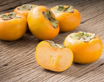Puede incluir: Cinco caquis naranjas maduros sobre una superficie de madera. Un caqui está cortado por la mitad, revelando la pulpa naranja.