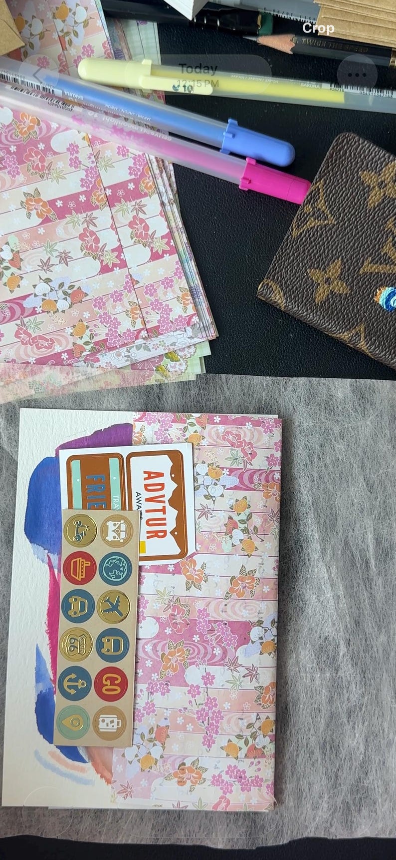 K&ouml;nnte beinhalten: Eine Sammlung von Schreibwaren, darunter Papier mit floralem Muster, Aufkleber und Stifte. Das Papier hat ein rosa-wei&szlig;es Blumenmuster. Eine braune, gemusterte Geldb&ouml;rse ist ebenfalls zu sehen.