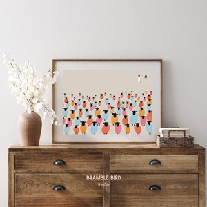 Op de afbeelding: Een ingelijste print van een kleurrijke illustratie van een kudde schapen met een enkele figuur die ervoor staat. De schapen zijn in verschillende tinten roze, blauw en oranje. De achtergrond is lichtbeige. De print is getiteld "Bramble Bird Creative."