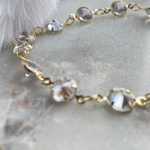 Puede incluir: Un brazalete de cadena de oro con piedras de cristal transparentes. Las piedras son redondas y facetadas, y est&aacute;n engastadas en un engaste de metal dorado.