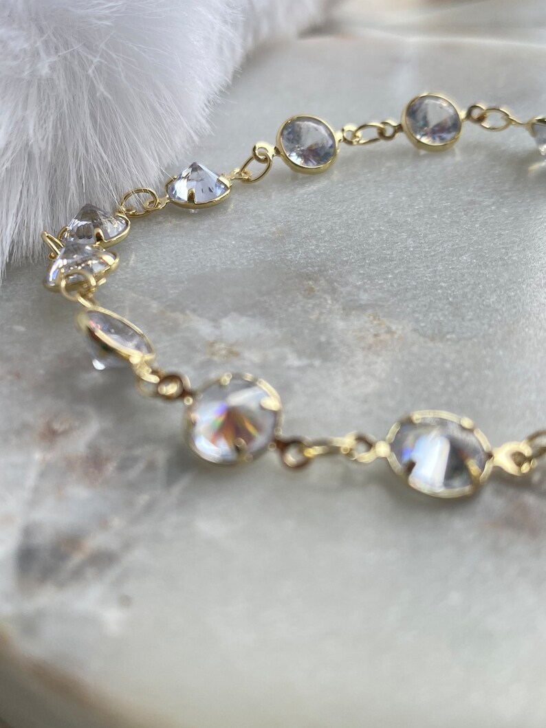 Puede incluir: Un brazalete de cadena de oro con piedras de cristal transparentes. Las piedras son redondas y facetadas, y est&aacute;n engastadas en un engaste de metal dorado.