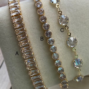Puede incluir: Tres pulseras de oro con piedras de cristal transparente. Las pulseras est&aacute;n etiquetadas como A, B y C. La pulsera A tiene piedras rectangulares, la pulsera B tiene piedras redondas y la pulsera C tiene piedras redondas m&aacute;s grandes.