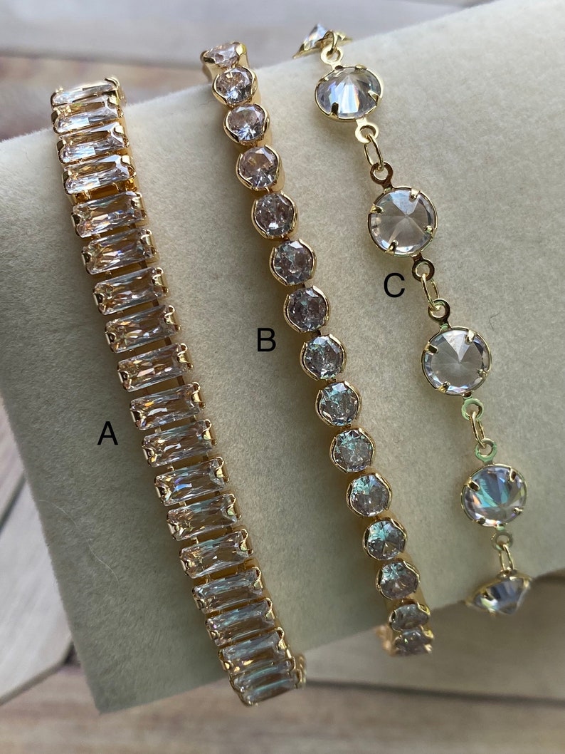 Puede incluir: Tres pulseras de oro con piedras de cristal transparente. Las pulseras est&aacute;n etiquetadas como A, B y C. La pulsera A tiene piedras rectangulares, la pulsera B tiene piedras redondas y la pulsera C tiene piedras redondas m&aacute;s grandes.