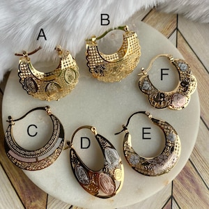 May include: Six pairs of gold hoop earrings with intricate designs. The earrings are made of three different shades of gold, including yellow, white, and rose gold. Each pair features a different design, including a floral pattern, a geometric pattern, and a religious icon.