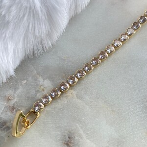 Puede incluir: Un brazalete de cadena dorada con piedras redondas transparentes. El brazalete tiene un cierre de broche.