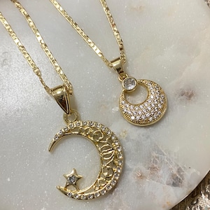 May include: Two gold necklaces with crescent moon pendants. One pendant features a small star and the other has a single round stone.