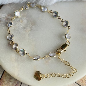 Puede incluir: Un brazalete de oro con un dije de coraz&oacute;n y piedras redondas transparentes.