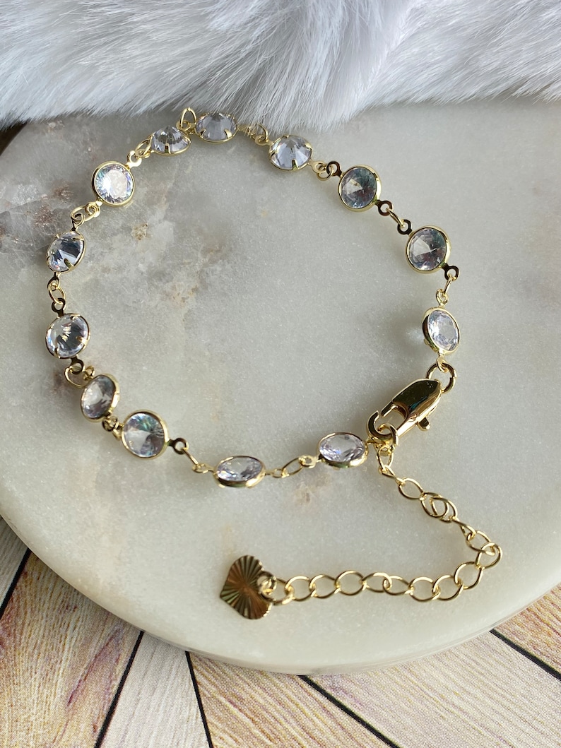Puede incluir: Un brazalete de oro con un dije de coraz&oacute;n y piedras redondas transparentes.