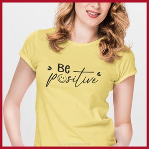 K&ouml;nnte beinhalten: Gelbes T-Shirt mit dem schwarzen Schriftzug "Be positive" und einem Smiley. Das Shirt hat kurze &Auml;rmel und einen Rundhalsausschnitt. Der Text ist mittig auf der Vorderseite des Shirts platziert.