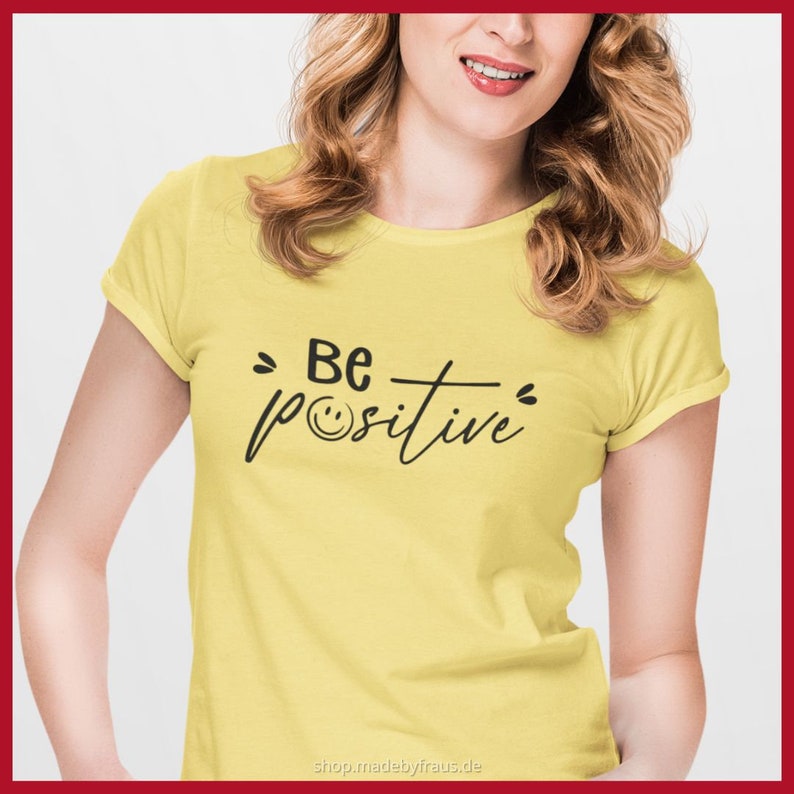 K&ouml;nnte beinhalten: Gelbes T-Shirt mit dem schwarzen Schriftzug "Be positive" und einem Smiley. Das Shirt hat kurze &Auml;rmel und einen Rundhalsausschnitt. Der Text ist mittig auf der Vorderseite des Shirts platziert.
