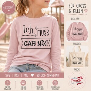 Könnte beinhalten: Hellrosa Sweatshirt mit dem deutschen Text "Ich muss gar nix!" in Schwarz. Das langärmlige Sweatshirt wird von einer Person getragen. Das Bild zeigt auch einen rosa Pullover und eine Tragetasche mit demselben Text.