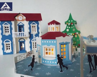 May include: A papercraft winter scene featuring a blue and white building, a red-roofed kiosk, a green Christmas tree, and two figures ice skating on a white snowflake patterned surface.