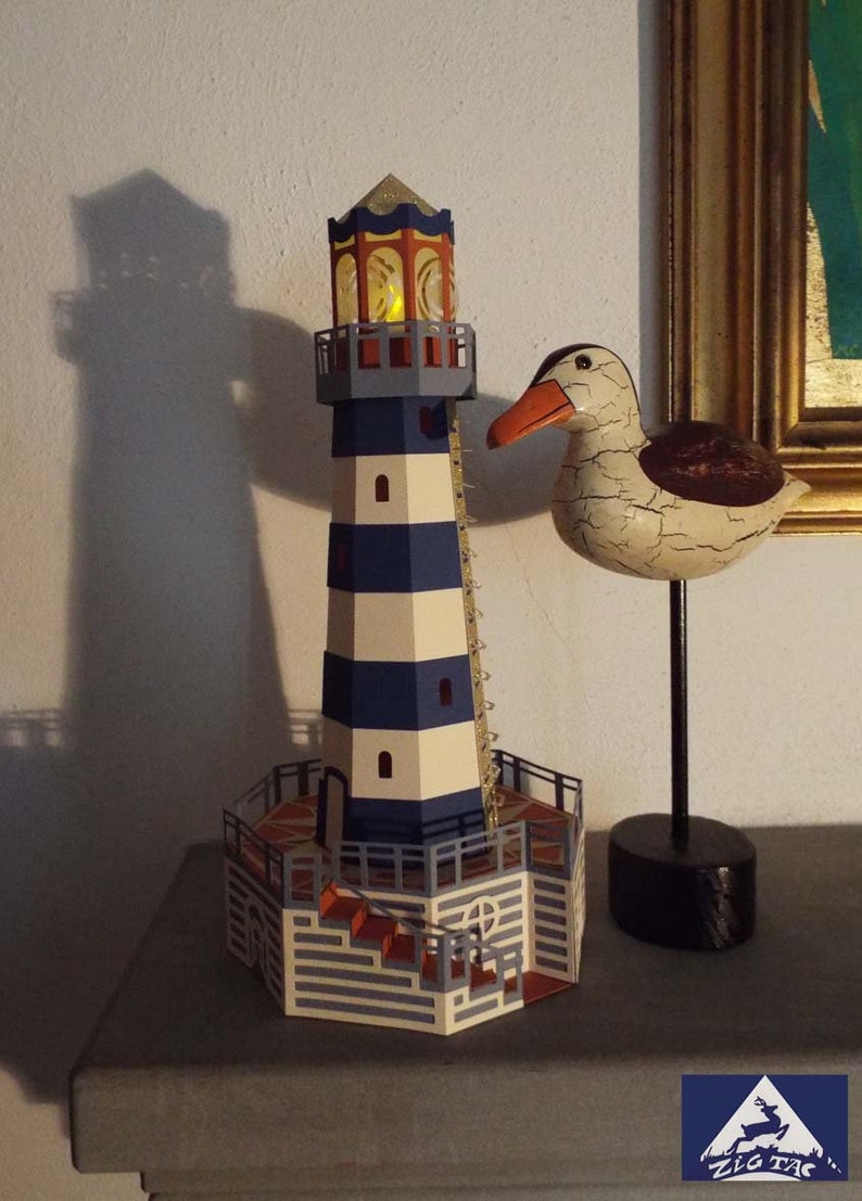 May include: A blue and white striped lighthouse with a yellow light in the top window. The lighthouse is on a wooden base with a brown and orange tiled floor. A white wooden seagull with a black beak is on a black stand to the right of the lighthouse.