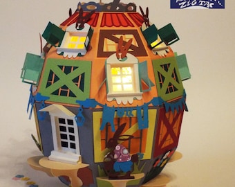 Könnte beinhalten: Ein farbenfrohes Papierbastel-Haus in Form eines Eies mit einem skurrilen Design. Das Haus hat Fenster, eine Tür und ein Dach mit einer Wetterfahne. Außerdem befinden sich kleine Papierhasen und Blumen um die Basis des Hauses. Das Haus wurde von Zig Zag hergestellt.