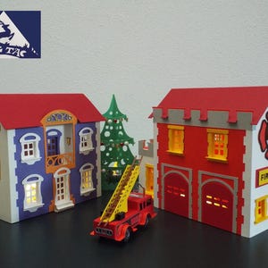 May include: A red and white fire station with a ladder truck in front. The fire station has two garage doors and a sign that says "Fire Dept.". There is a small, blue and white house with a red roof to the left of the fire station.