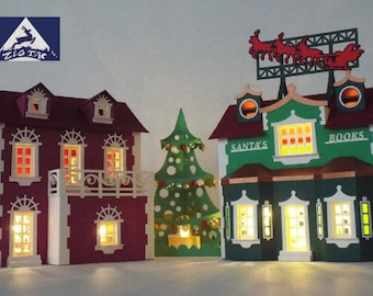 May include: A papercraft Christmas village scene with a red house, a green house with "Santa's" and "Books" signs, and a green Christmas tree with white and gold ornaments.