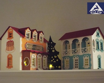 May include: A papercraft village scene with three buildings, a bakery, a house with a balcony, and a building with a white facade. The bakery has a sign that reads "Holidays Bakery".