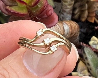 May include: A gold ring with three small diamonds set in a wavy band.