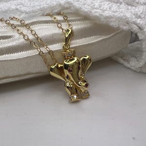 Może przedstawiać: Złoty naszyjnik z wisiorkiem w kształcie słonia. Słoń ma czerwone oczy i jest ozdobiony małymi, przezroczystymi kamieniami szlachetnymi. Łańcuszek naszyjnika jest również złoty i delikatny. Wisiorek ma około 2,5 cm wysokości.