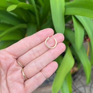 May include: A small, circular gold hoop earring with a thin wire post and a simple hinge closure mechanism. The earring features a polished metallic finish and a classic, minimalist round shape, designed to be worn as a single piece of jewelry.