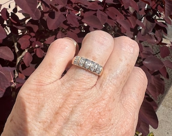 Puede incluir: Un anillo dorado con múltiples filas de pequeñas piedras preciosas transparentes. El anillo se lleva en un dedo, con un fondo de follaje rojo oscuro.