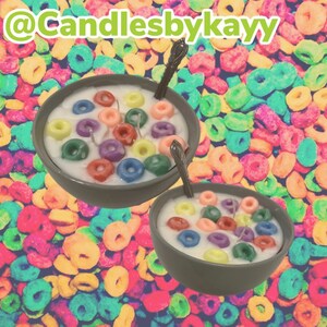 Puede incluir: Dos cuencos de cerámica gris llenos de cera blanca, velas con forma de cereales de colores y cucharas plateadas. El fondo es un vibrante patrón de piezas de cereales de colores. El texto "@Candlesbykayy" está en la esquina superior izquierda.