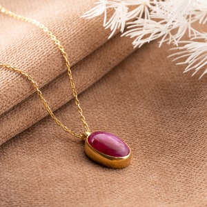 May include: A gold chain necklace with a red oval gemstone pendant.