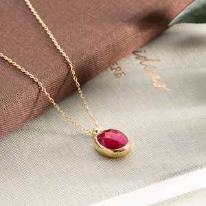 May include: A gold chain necklace with a red gemstone pendant. The pendant is oval shaped and has a faceted design.
