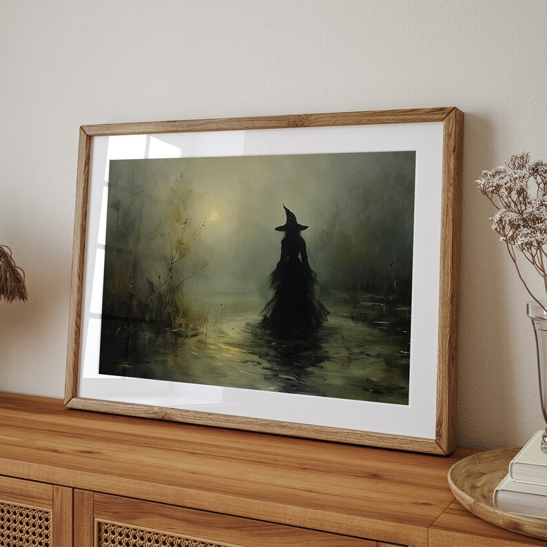 May include: A framed art print depicts a silhouetted figure in a witch's hat and gown wading through water. The artwork has a muted color palette of greens, yellows, and blacks, creating a mysterious and atmospheric scene. The print is displayed in a wooden frame.