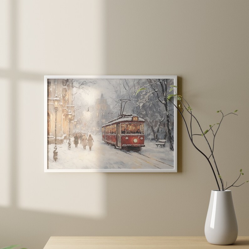 May include: Framed art print of a winter scene featuring a red trolley car on a snow-covered street. The artwork depicts figures walking along the sidewalk, with buildings and trees in the background. The painting has a soft, muted color palette.