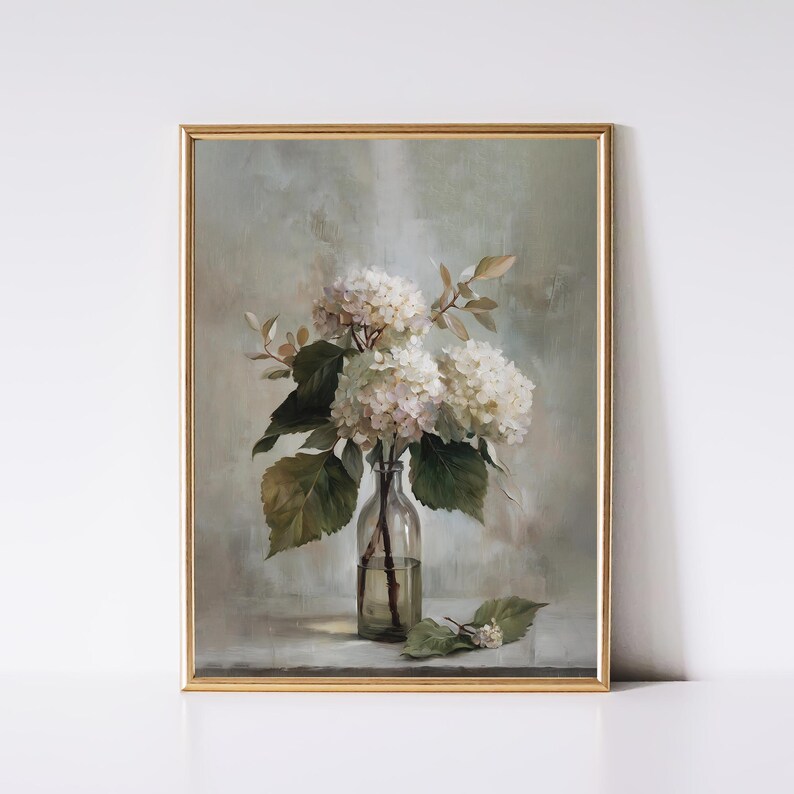 May include: A framed art print featuring a still life of white hydrangea flowers in a clear glass bottle. The artwork has a soft, muted color palette with green leaves and a gold frame. The painting evokes a vintage, botanical theme.