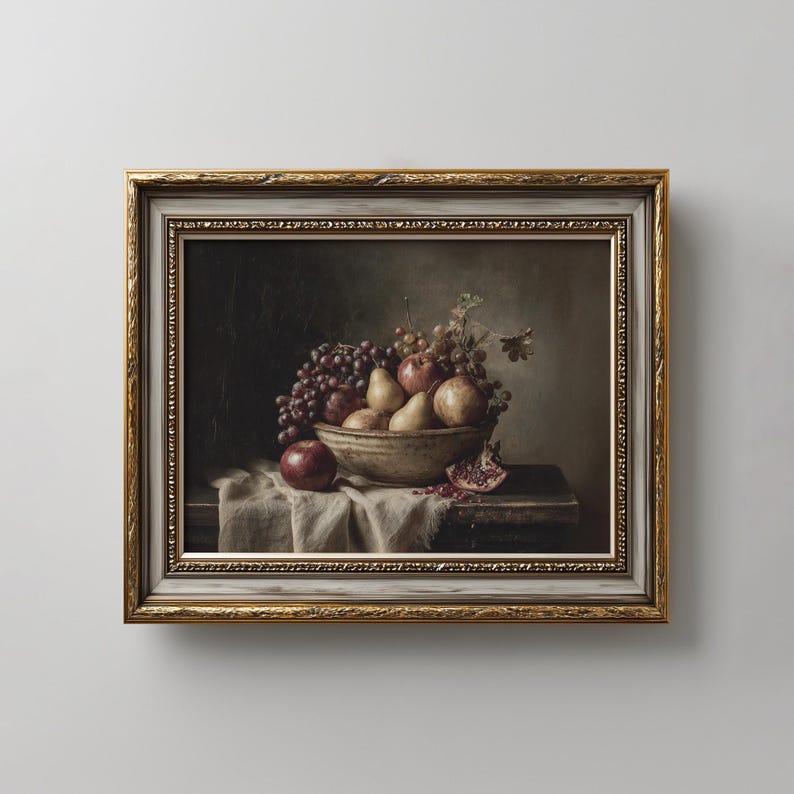 May include: A framed still life oil painting depicting a ceramic bowl filled with red grapes, pears, and apples resting on a draped white cloth. A single red apple sits beside the bowl, and a halved pomegranate lies on the dark wooden surface.