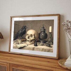 May include: A framed print featuring a still life with a skull, a black raven, and antique objects. The skull is centered, with a raven perched on a book to the left. A candle, lantern, and other items complete the composition.