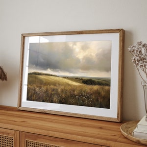 Peut inclure: Une peinture de paysage encadr&eacute;e repr&eacute;sentant un champ vert vallonn&eacute; avec un ciel nuageux. La peinture est dans un cadre en bois et est accroch&eacute;e &agrave; un mur.