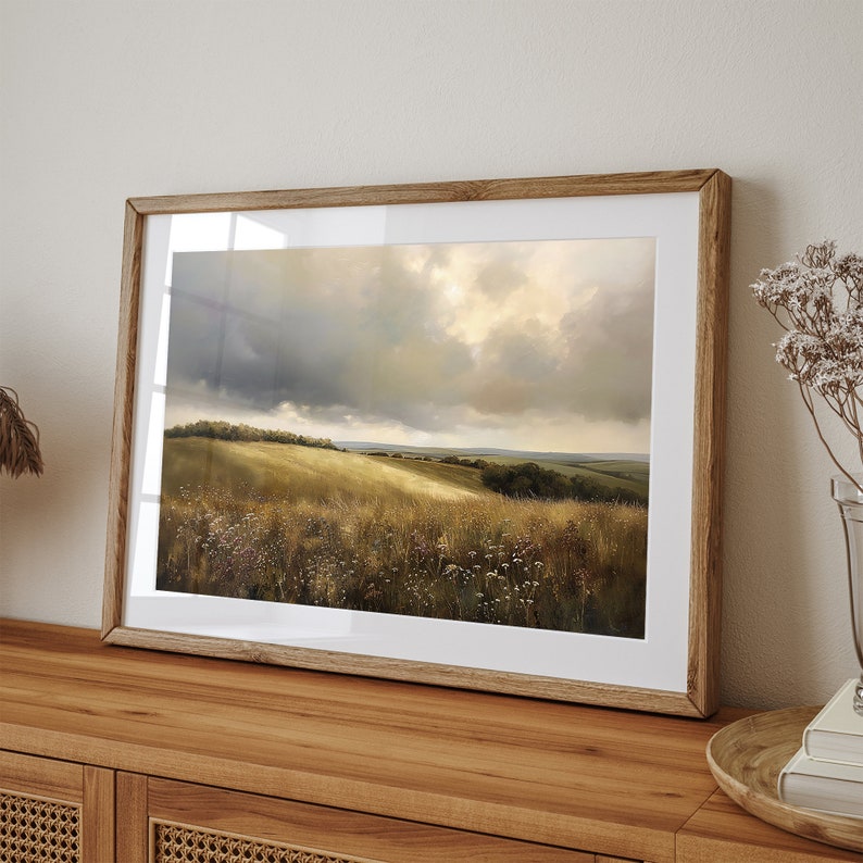 Peut inclure: Une peinture de paysage encadr&eacute;e repr&eacute;sentant un champ vert vallonn&eacute; avec un ciel nuageux. La peinture est dans un cadre en bois et est accroch&eacute;e &agrave; un mur.