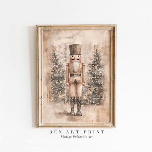 May include: Framed vintage art print with a watercolour illustration of a nutcracker soldier. The nutcracker is in a tan uniform with a black top hat and boots. Two Christmas trees with twinkling lights are in the background. The text "RÉn Art Print Vintage Printable Art" is at the bottom.
