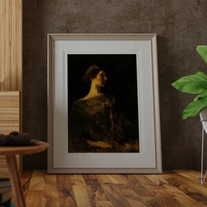 May include: Framed portrait of a woman in profile, rendered in dark tones with a focus on the face and shoulders. The artwork is displayed in a light-colored frame, set against a dark background, and resting on a wooden floor.