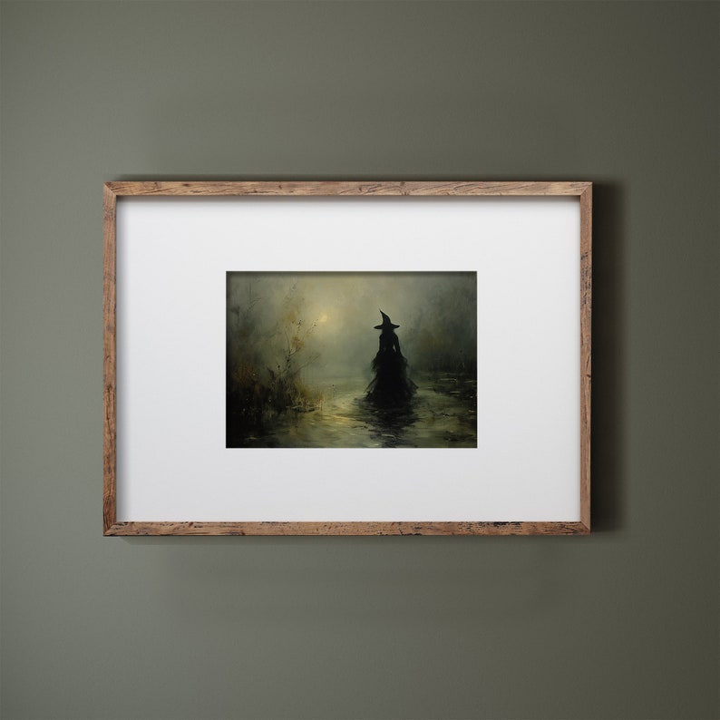 May include: A framed art print depicts a silhouetted figure in a witch's hat and flowing gown wading through water. The artwork is set in a misty, atmospheric landscape with muted greens and browns, and a soft, golden light.