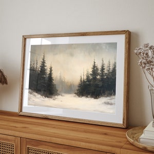 May include: A framed painting of a snowy forest scene with dark green trees and a white snowy ground. The painting is in a light brown wooden frame.