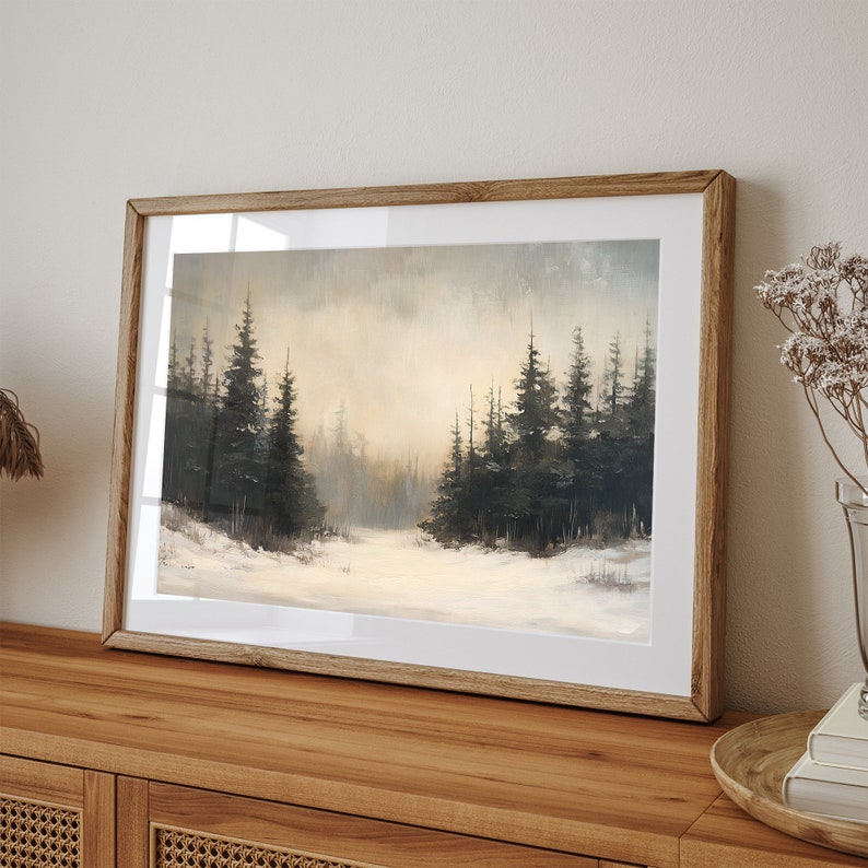 May include: A framed painting of a snowy forest scene with dark green trees and a white snowy ground. The painting is in a light brown wooden frame.