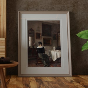May include: A framed painting depicting a woman in a dark dress sitting in a chair and reading a book. The painting is set in a room with a table and chairs, and there are several framed pictures on the walls.