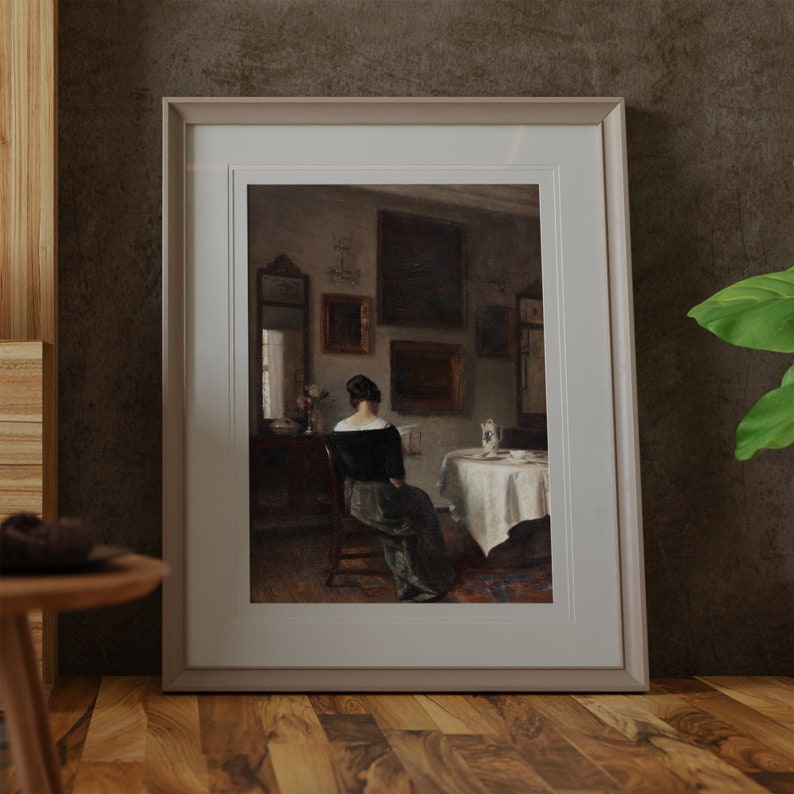 May include: A framed painting depicting a woman in a dark dress sitting in a chair and reading a book. The painting is set in a room with a table and chairs, and there are several framed pictures on the walls.