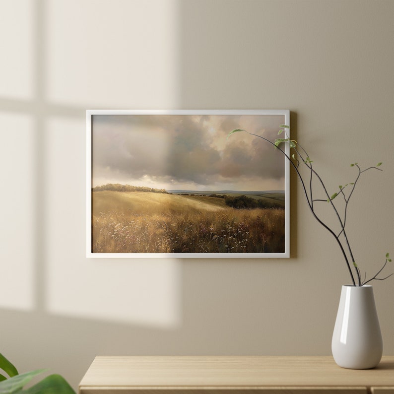 Peut inclure: Une peinture de paysage encadr&eacute;e repr&eacute;sentant un champ avec des collines vallonn&eacute;es et un ciel nuageux. La peinture est dans un cadre blanc et est accroch&eacute;e &agrave; un mur beige.