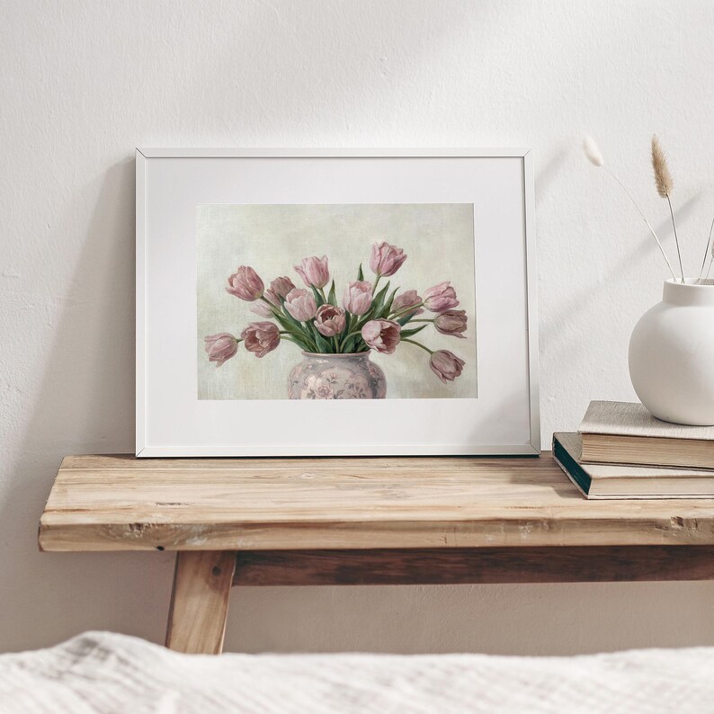 May include: A framed print of a still life featuring a bouquet of pink tulips in a decorative vase. The vase has a floral pattern and sits on a wooden surface. The artwork is displayed in a white frame.