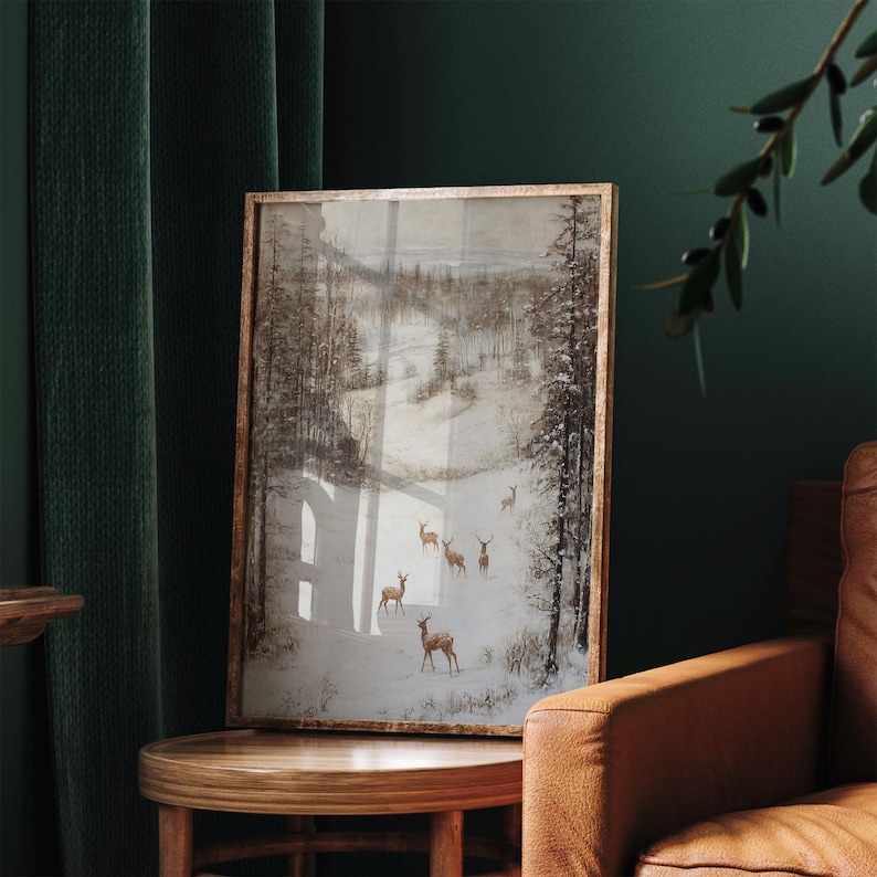 Op de afbeelding: Een ingelijste kunstafdruk met een winterlandschap met herten in een besneeuwd bos. Het kunstwerk heeft een vintage esthetiek met een houten frame. Het kleurenpalet omvat tinten bruin, wit en grijs, wat een serene en natuurlijke sfeer cre&euml;ert.