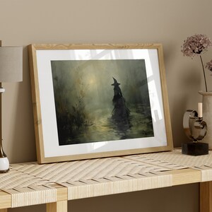 May include: Framed art print featuring a silhouetted figure in a witch's hat and flowing gown, wading through water. The artwork has a dark, atmospheric quality with muted greens and yellows, set in a wooden frame.